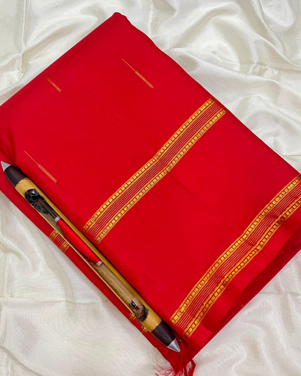 A folded bright red silk saree with gold zari borders and motifs, displayed on a white satin fabric background 