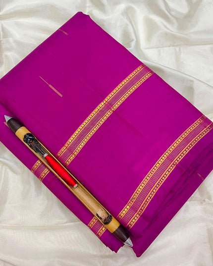 A folded magenta purple saree with gold zari borders, displayed on a white satin fabric background