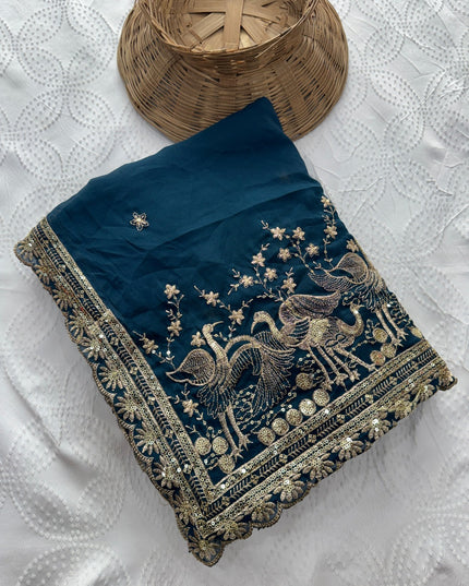 Folded teal Rangoli silk saree showing embroidered bird and floral motifs and an ornate border.