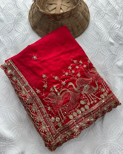Folded ruby red Rangoli silk saree showing embroidered bird and floral motifs and an ornate border.